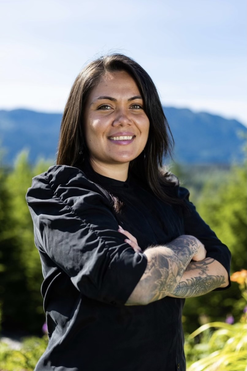 Lisa Grant standing outdoors in front of mountains and evergreens, arms crossed